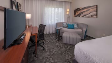 A hotel room with a bed, a desk with a computer, a chair, a sofa, and a TV.