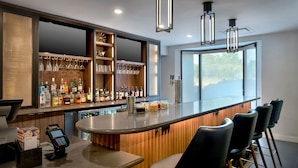 Un bar moderno con mostrador de madera, taburetes y una variedad de botellas de licor.