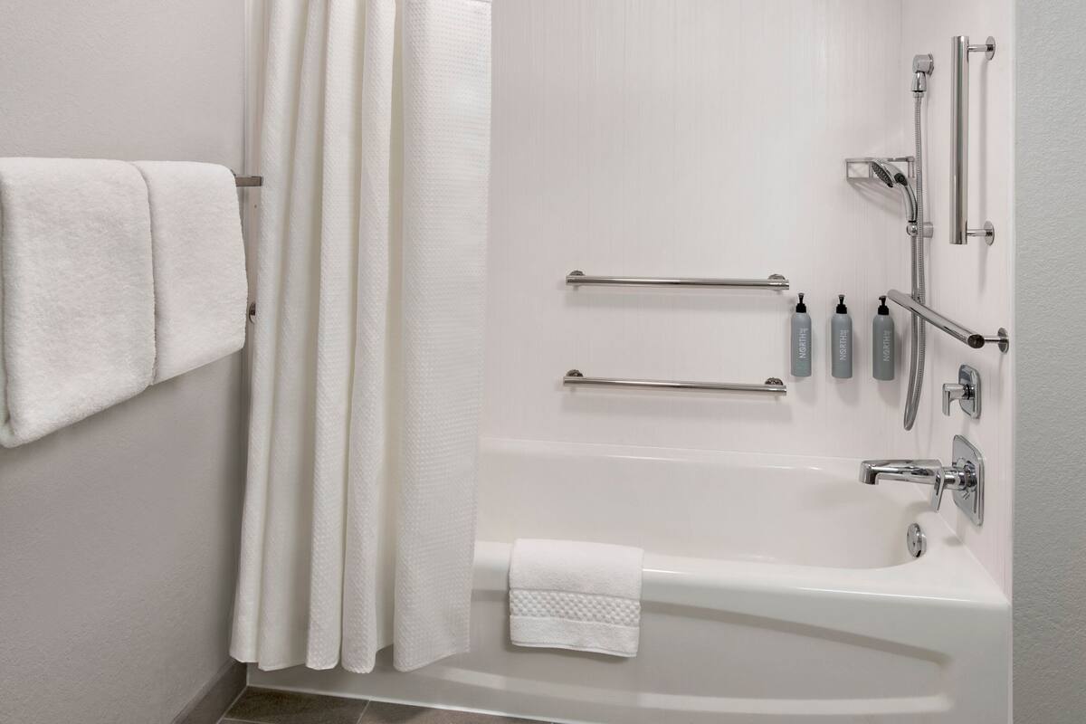 A modern bathroom with a white bathtub, grab bars, and handrails.