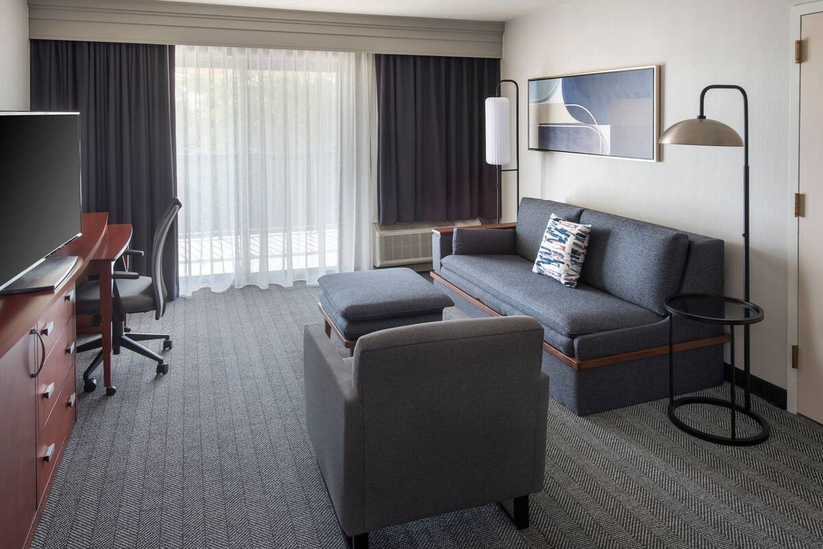 A hotel room with a sofa, a desk, a TV, a lamp, and a window with curtains.