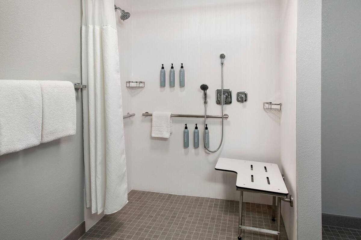 A small, modern bathroom with a shower, a towel rack, and a sink with a soap dispenser.