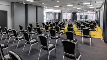 Un salón de conferencias con hileras de sillas, un atril y una gran pantalla que muestra 'PENTA HOTEL ROSTOCK'.