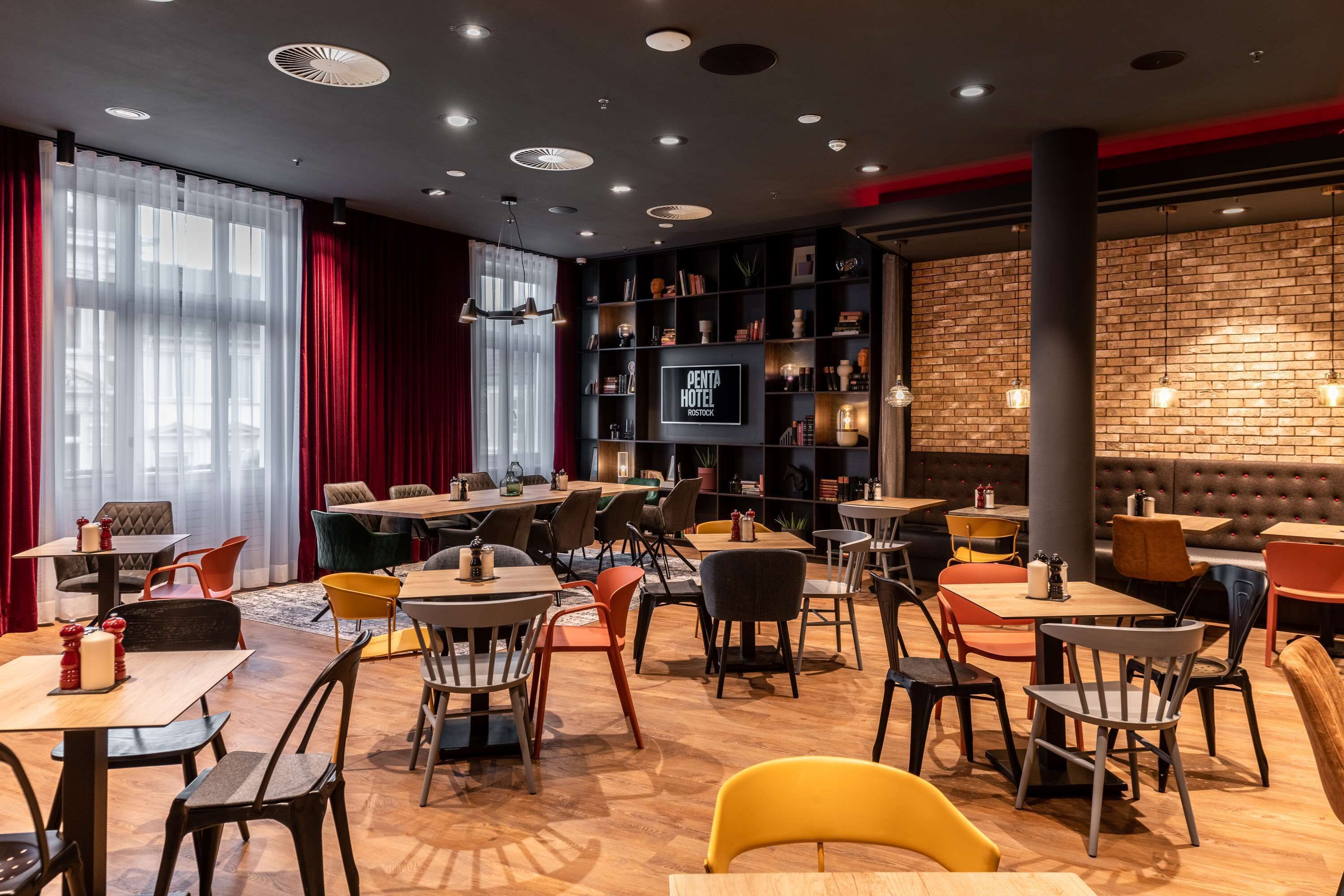 Un restaurant moderne doté de nombreuses tables et chaises, d’un écran de télévision et d’un mur en briques.