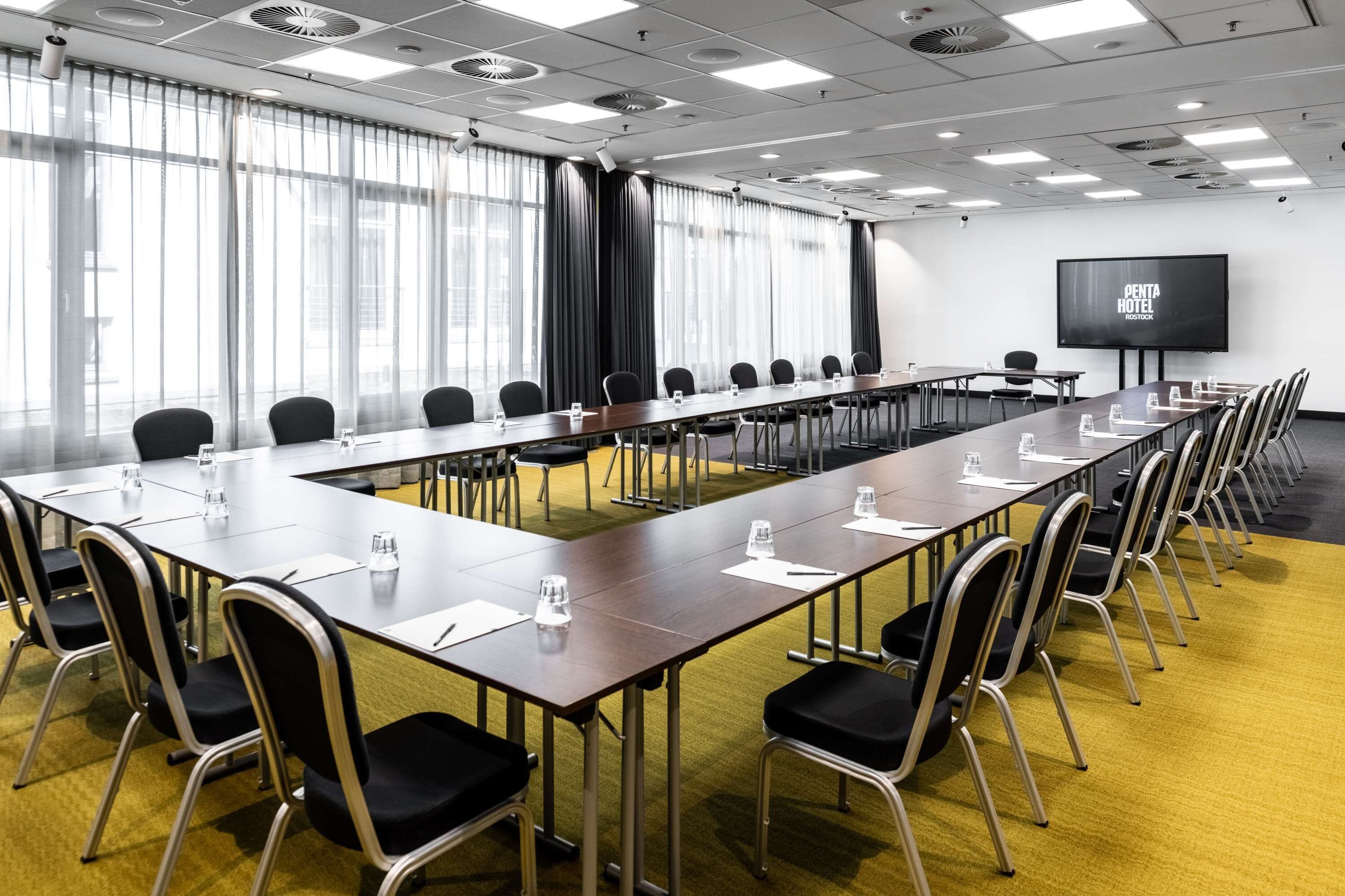 A conference room with a long table, chairs, a projector screen, and a large window with curtains.