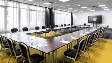 A conference room with a long table, chairs, a projector screen, and a large window with curtains.