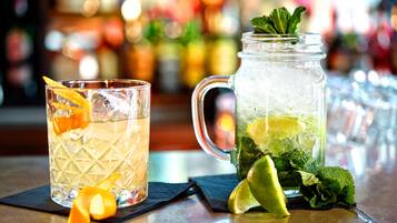 Un bar avec un verre et une carafe contenant une boisson décorée d’une tranche de citron vert et de quelques feuilles de menthe, le tout sur un fond flou de bouteilles.