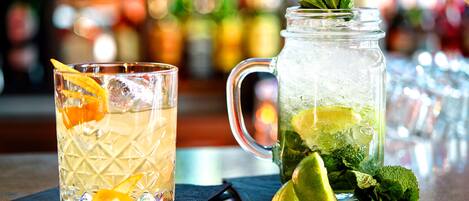 En bardisk med ett glas och en kanna fylld med en dryck, garnerad med lime och mynta, och en suddig bakgrund bestående av flaskor.