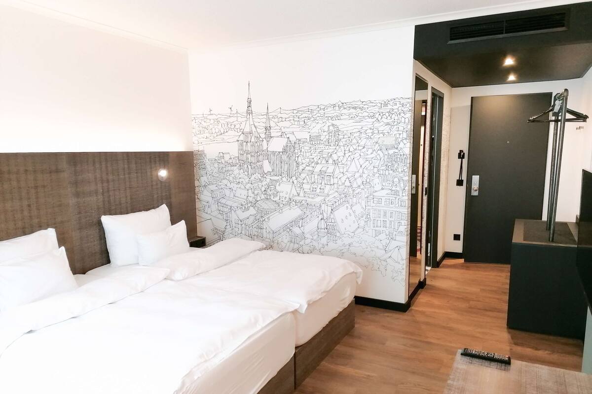 A hotel room with a large bed, a headboard, a wall mural, a shower area, and a desk.