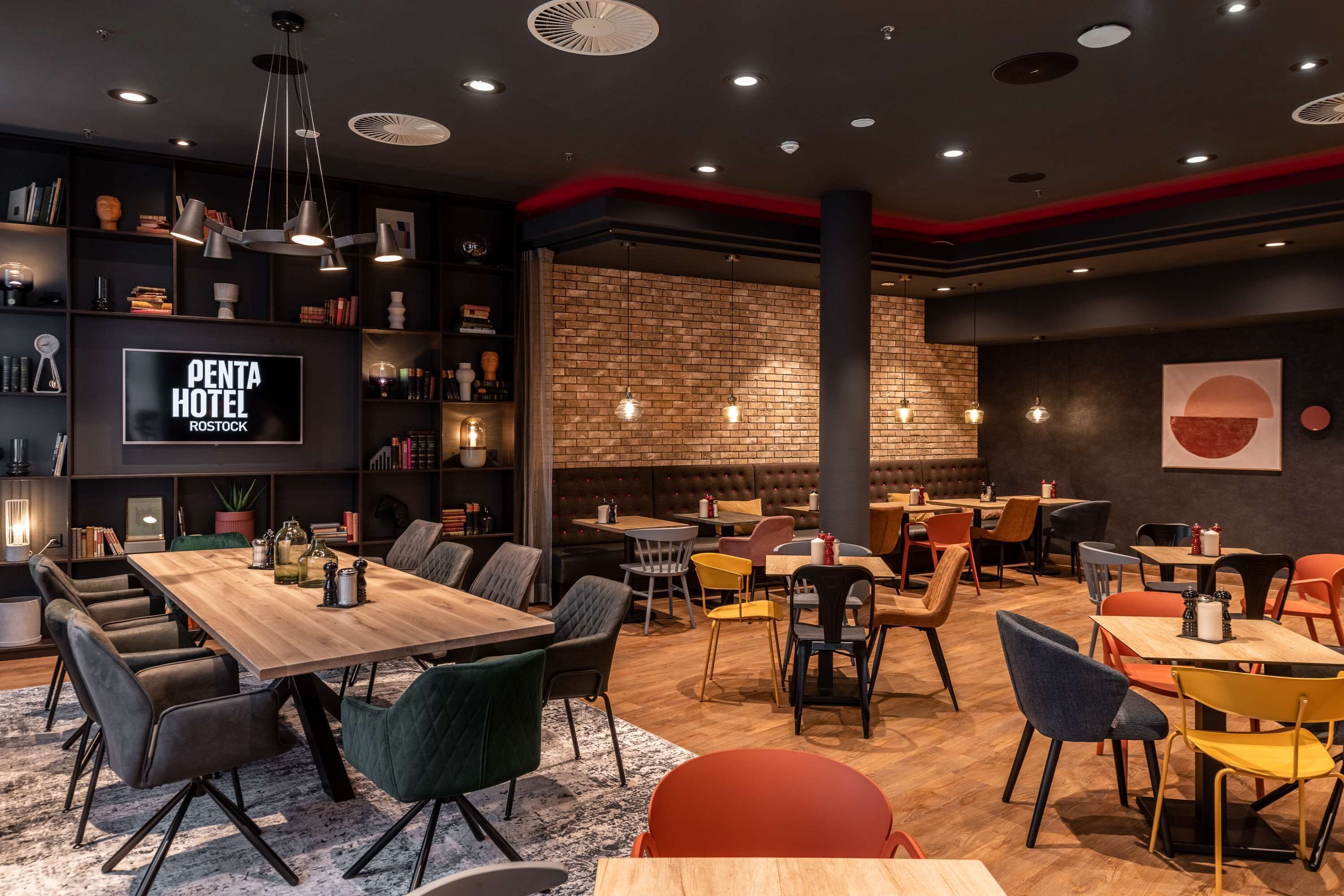 Un restaurante moderno con pared de ladrillo, mesas de madera y sillas coloridas.