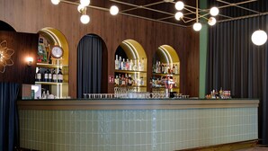Un espace bar avec un comptoir recouvert de carreaux verts, de nombreuses étagères remplies de bouteilles et une horloge au mur.