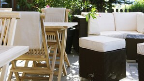 Un espace patio aménagé avec des chaises en bois et un canapé en osier, tous deux dotés de coussins blancs.