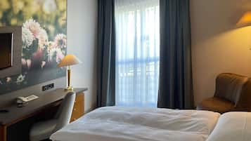 Hotellihuone, jossa on sänky, työpöytä lampun kanssa, televisio ja suuret ikkunat, joista on näkymä ulos.