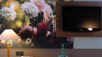 Ein Hotelzimmer mit einem Wandfernseher, einem Telefon, einer Lampe und einer dekorativen Glasflasche.