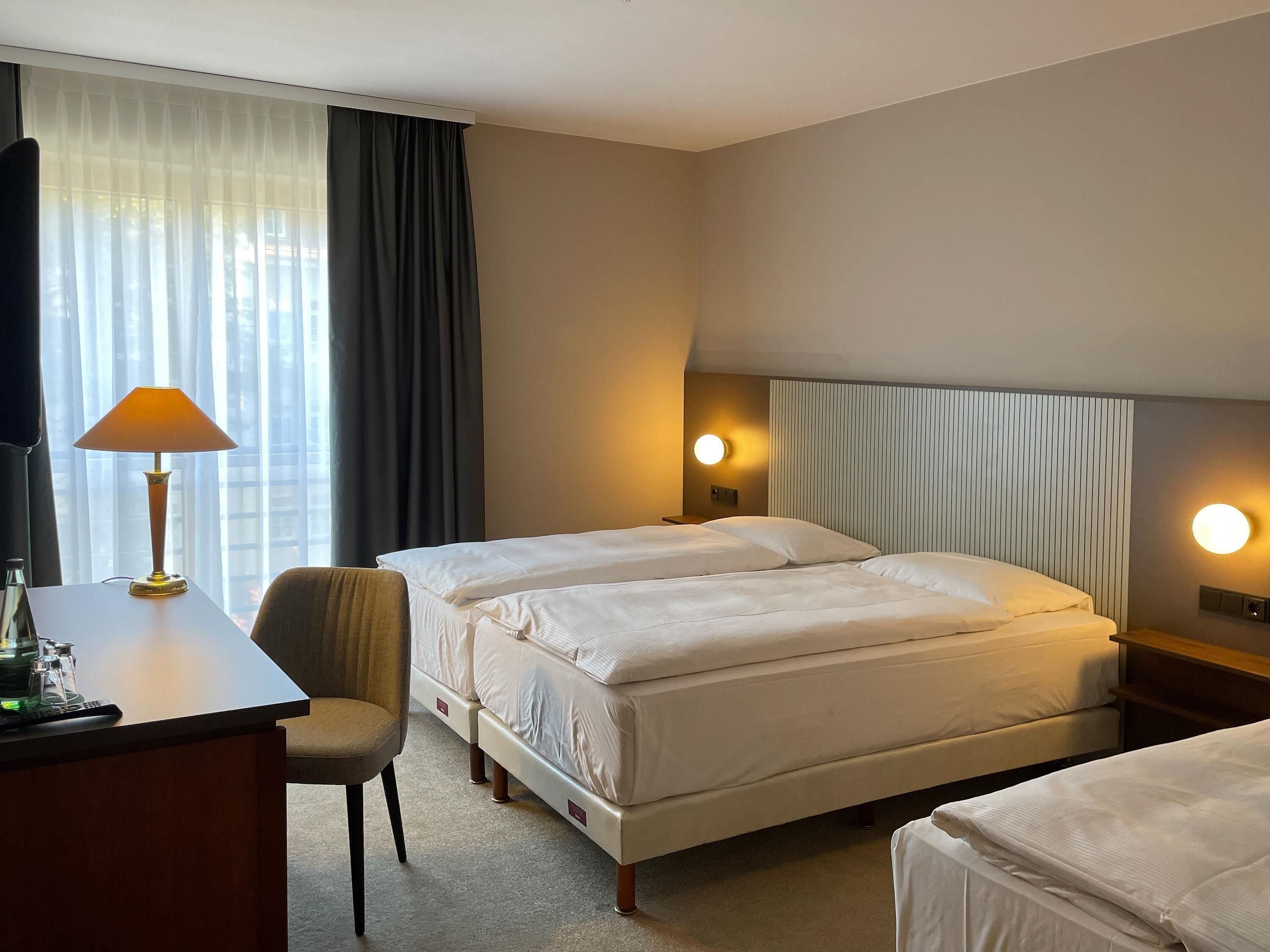 Une chambre d’hôtel avec deux lits, un bureau, une chaise et deux lampes de chevet.