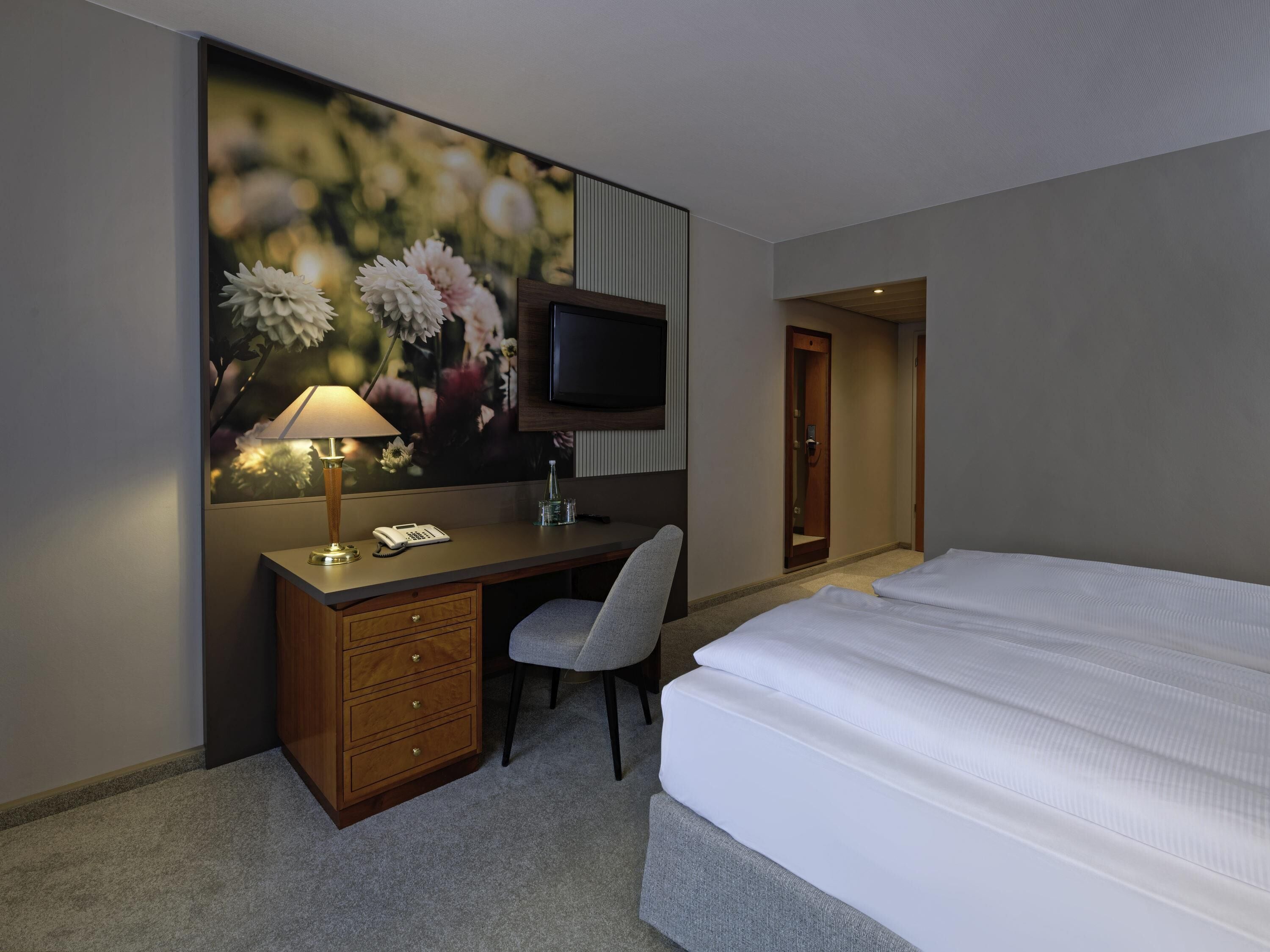 Ein Hotelzimmer mit Bett, Schreibtisch mit Lampe, Stuhl, Fernseher und einer Tür.