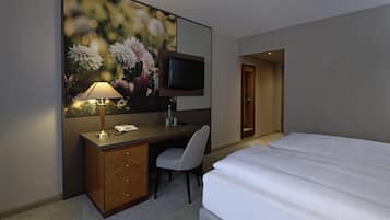 Ein Hotelzimmer mit Bett, Schreibtisch mit Lampe, Stuhl, Fernseher und einer Tür.