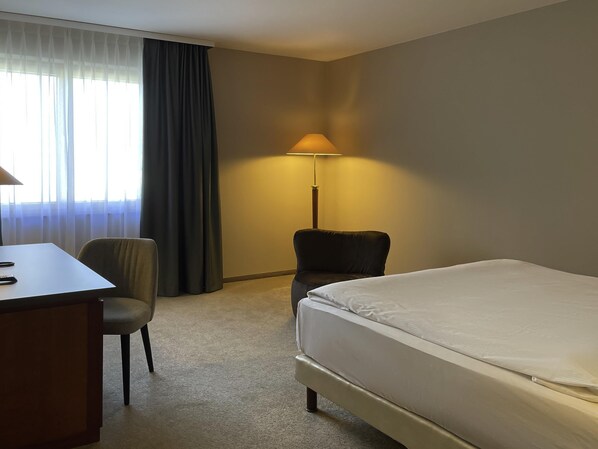A hotel room with a bed, a desk, a chair, a lamp, and a window with curtains.