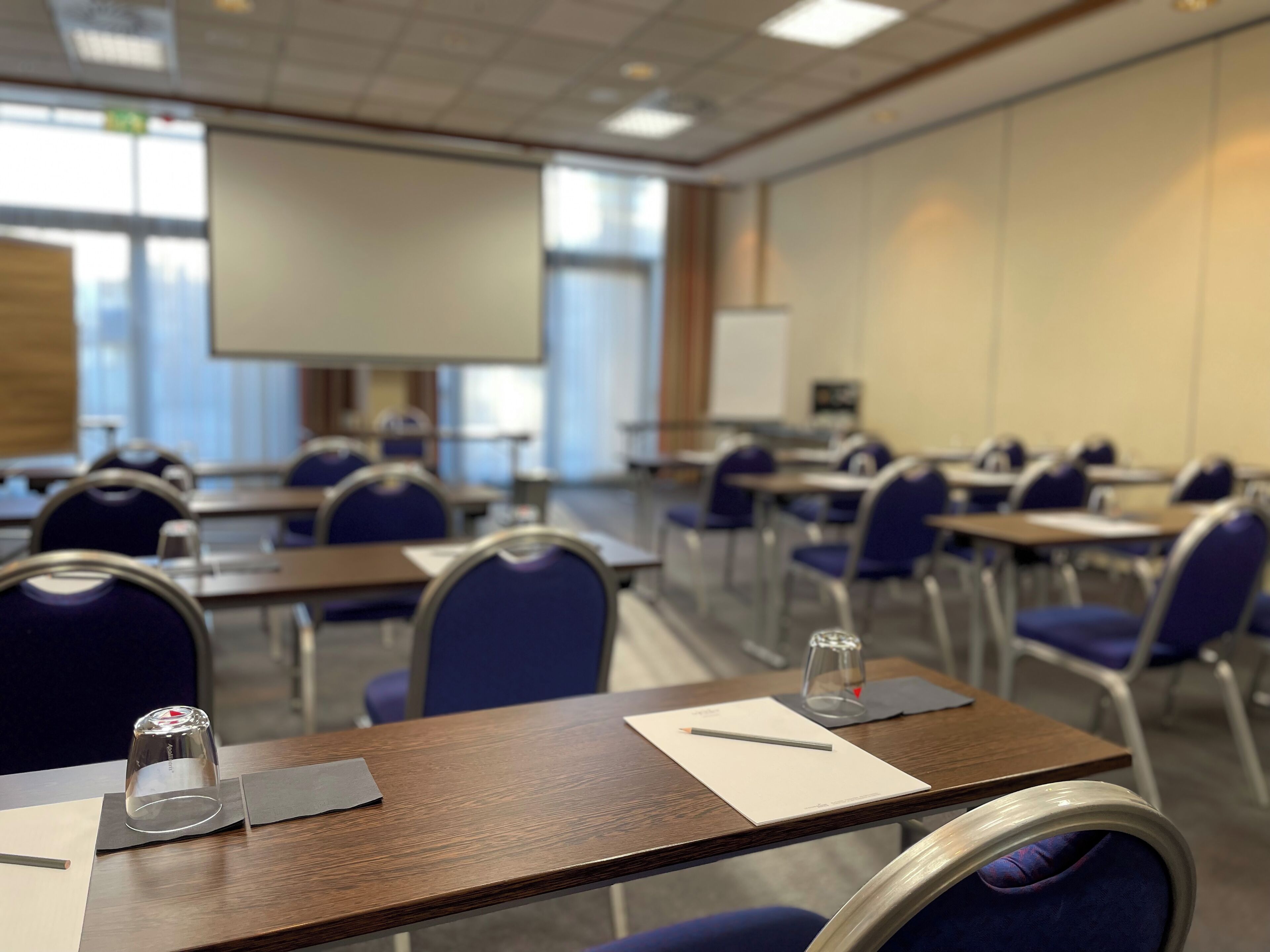 A conference room with tables, chairs, a projector screen, and a whiteboard.