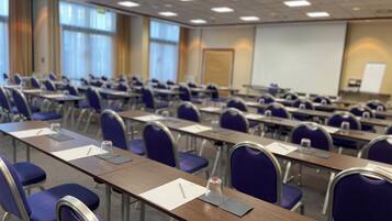 A conference room with rows of tables and chairs, a projector screen, and a whiteboard.