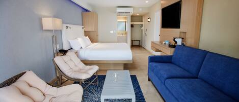 A hotel room with a bed, two chairs, a sofa, a coffee table, a TV, and a bathroom visible through an open door.