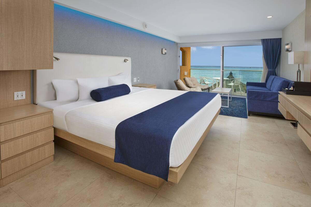 Ein modernes Hotelzimmer mit einem großen Bett, einem Schreibtisch, einem Stuhl und Blick aufs Meer.