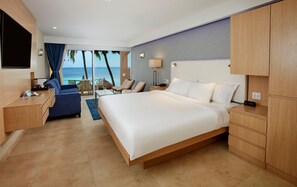 A hotel room with a large bed, a desk, a chair, a TV, and a view of the ocean.