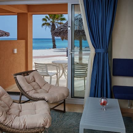 A balcony with wicker chairs, a table with a glass of red wine, and a view of the beach and ocean.