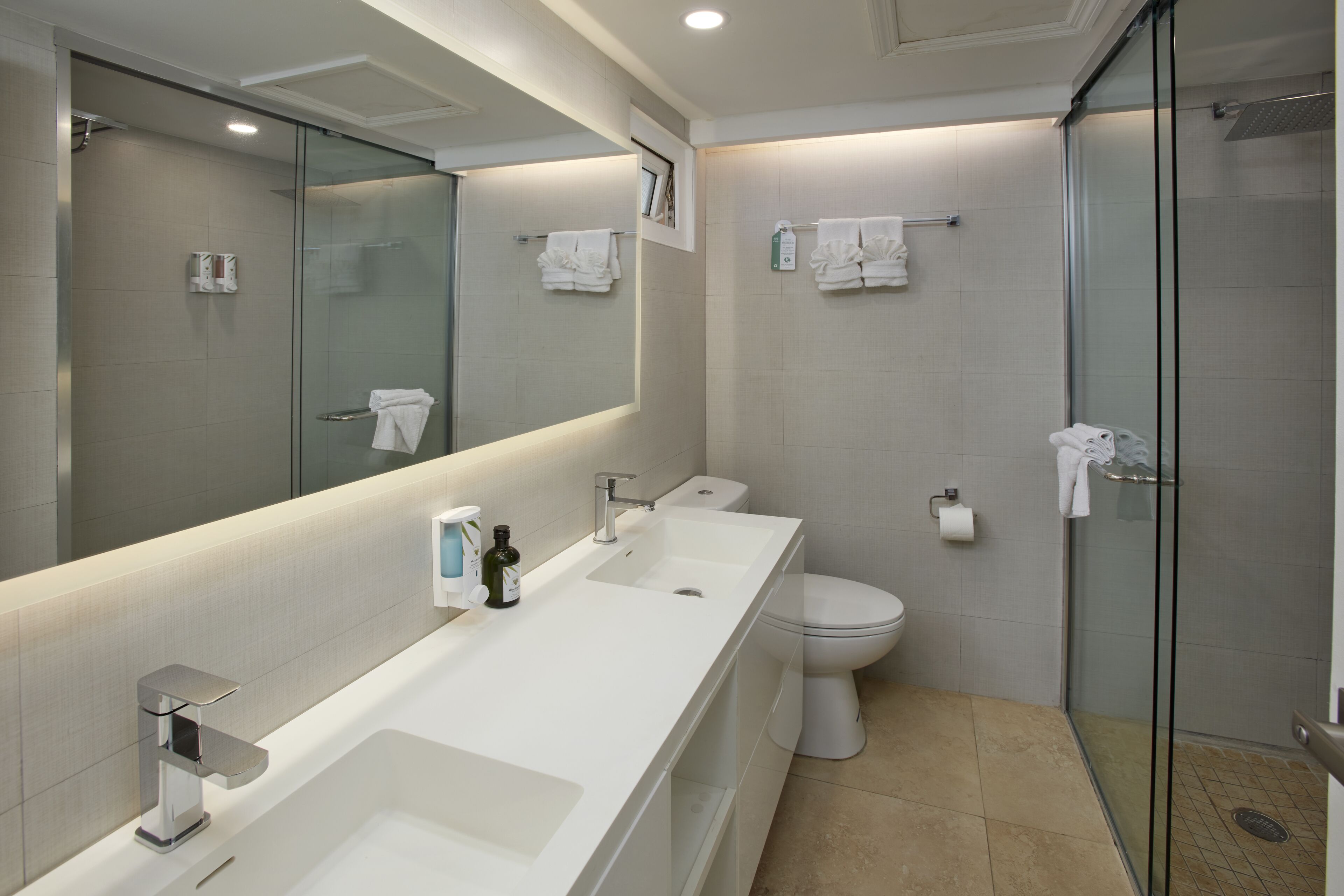 A modern bathroom with a long white sink, a toilet, and a glass-enclosed shower.