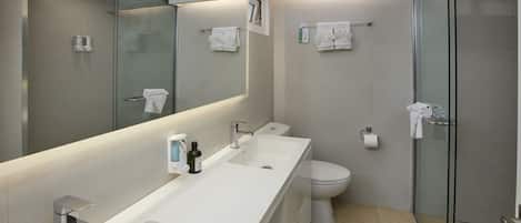 A modern bathroom with a long white sink, a toilet, and a glass-enclosed shower.