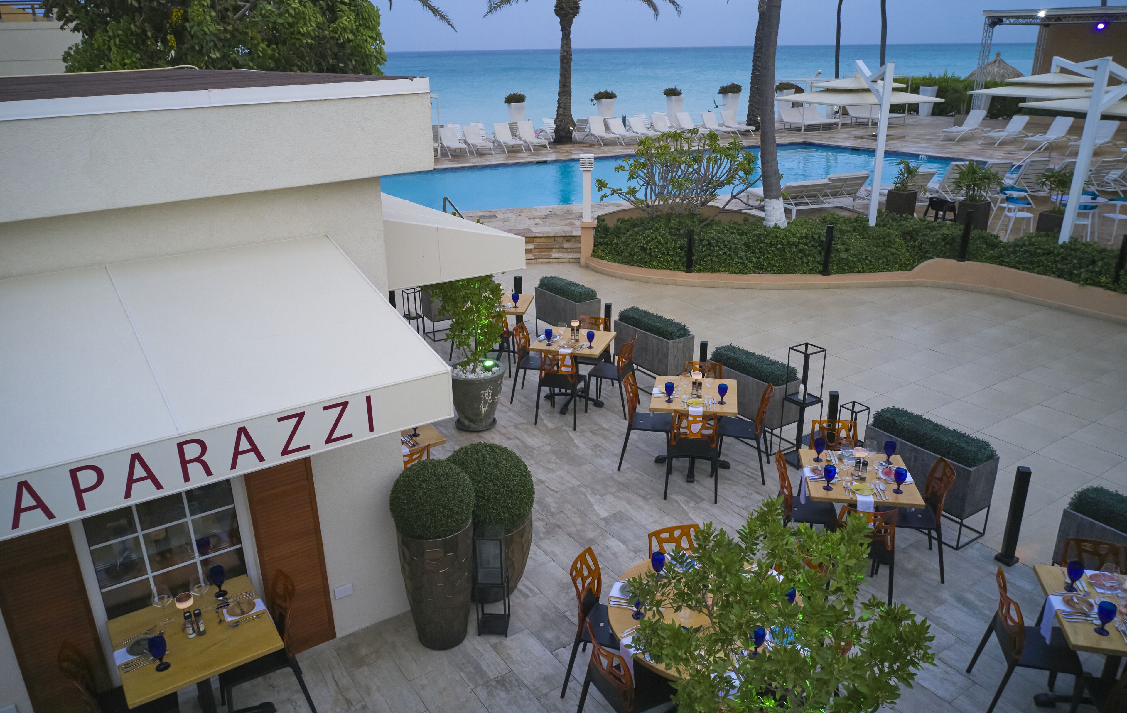 An outdoor dining area with tables and chairs, a pool, and a view of the ocean.