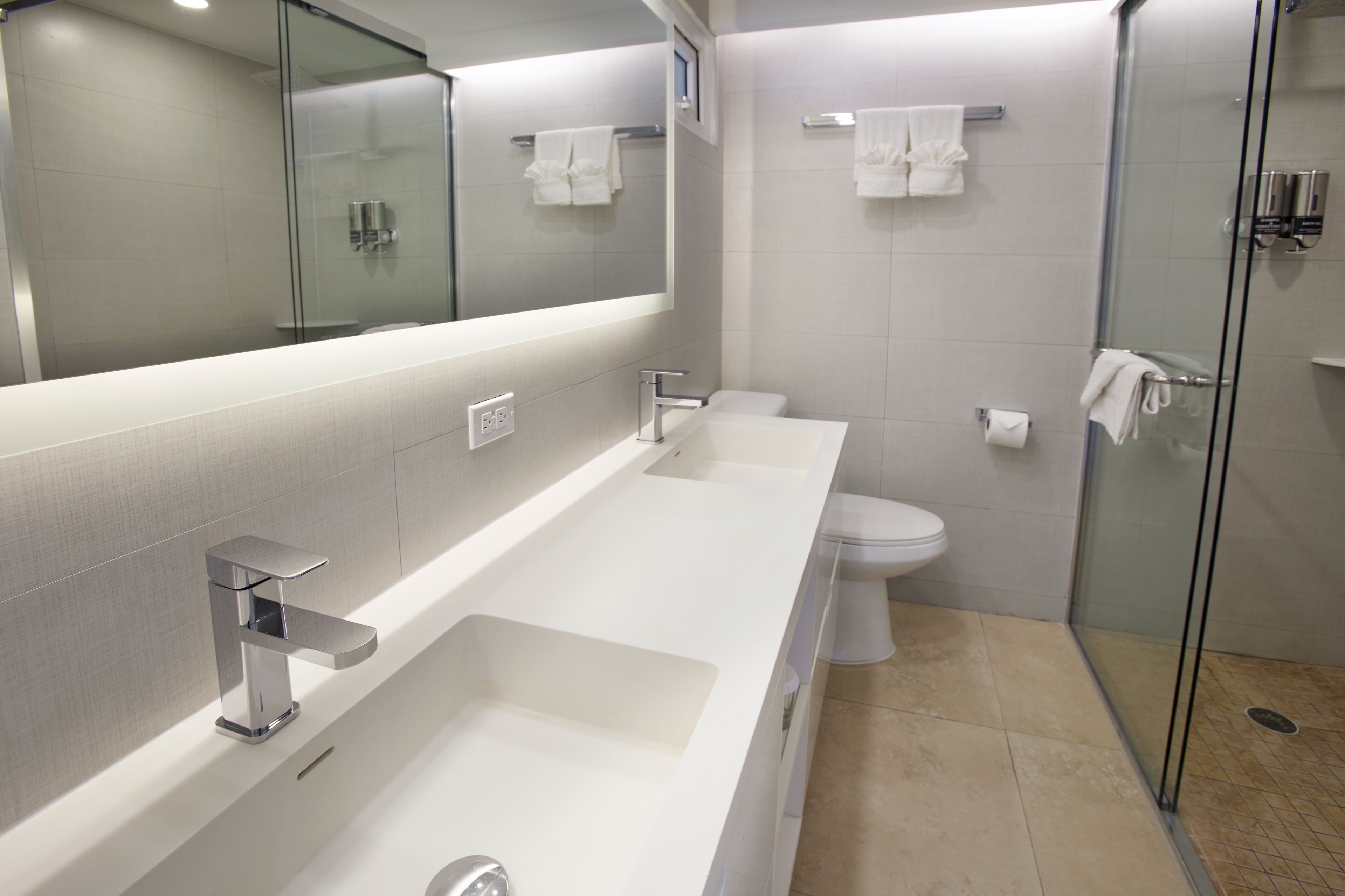 A modern bathroom with a large mirror, a white sink, a toilet, and a glass shower enclosure.