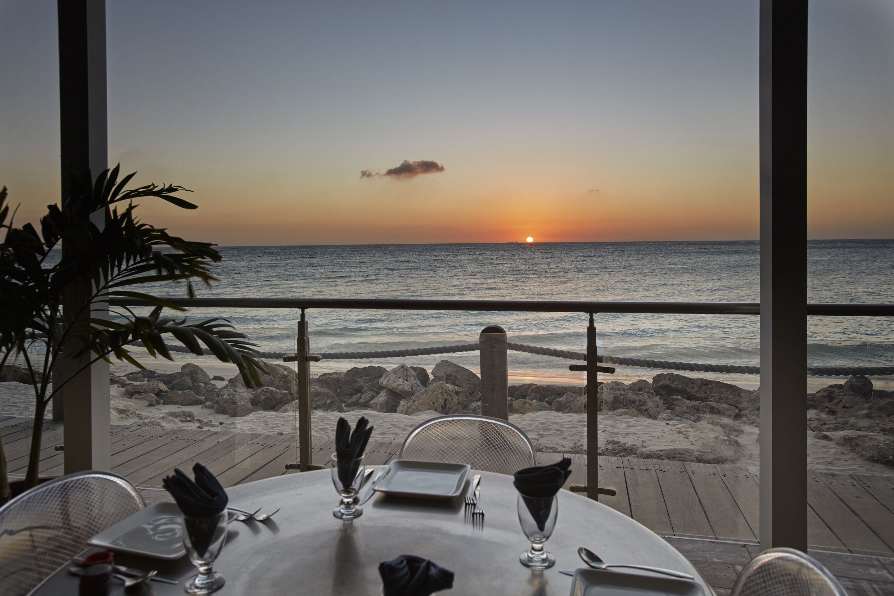 A table set for dining with a view of the ocean and sunset.