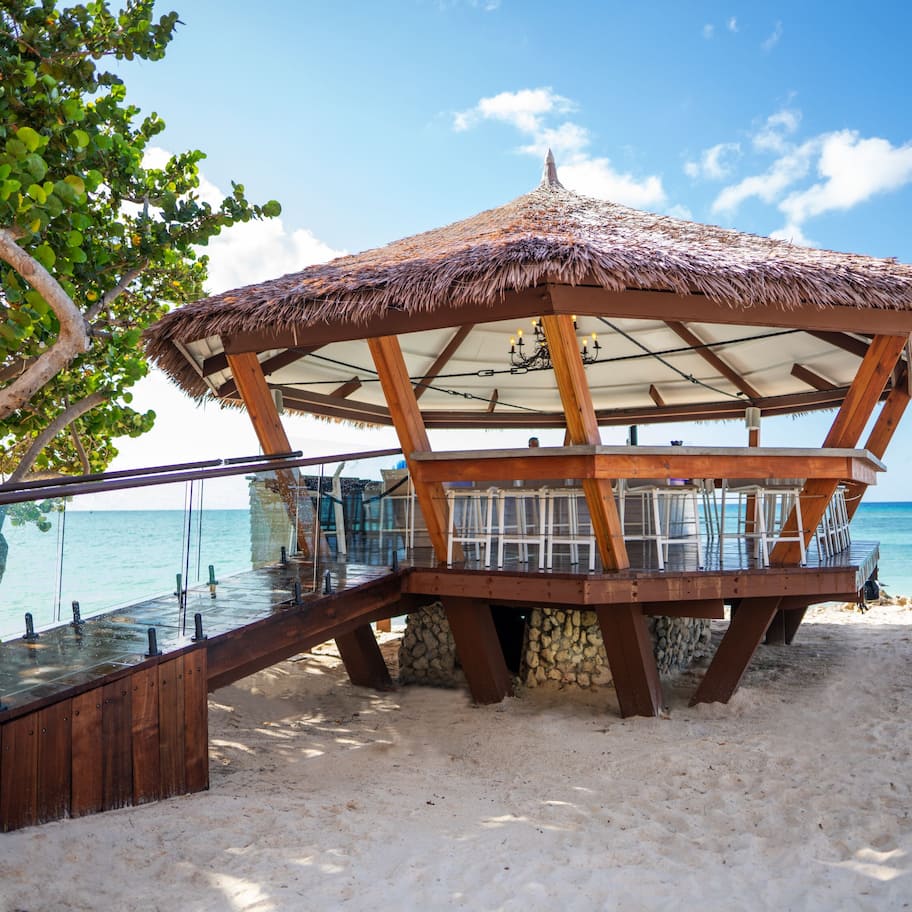 A wooden gazebo with a thatched roof overlooking a beach.