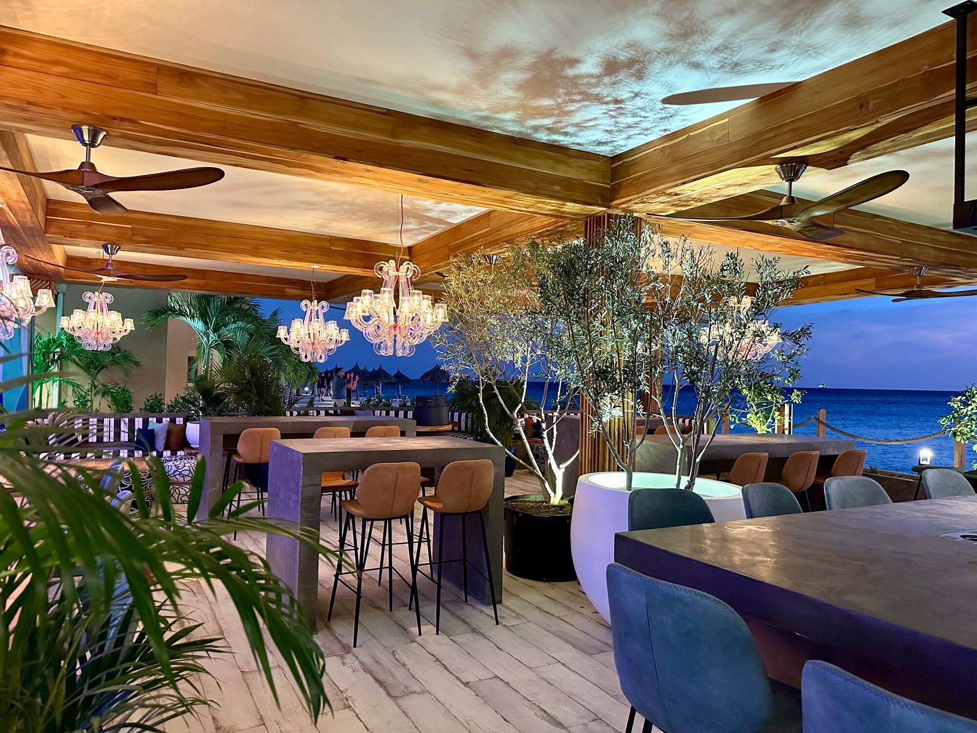 An outdoor dining area with wooden beams, ceiling fans, and modern lighting fixtures.