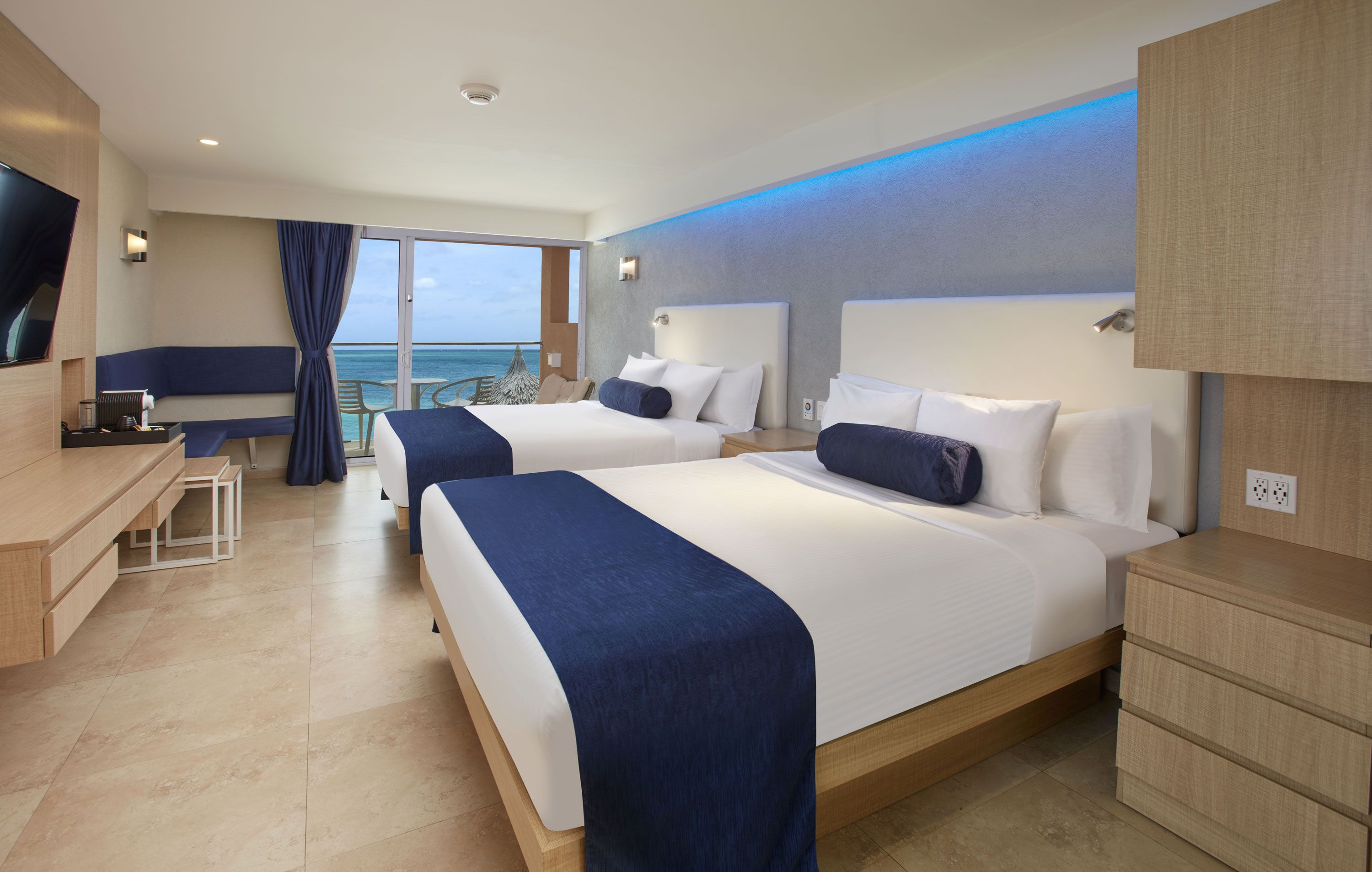 A hotel room with two beds, a desk, and a view of the ocean.