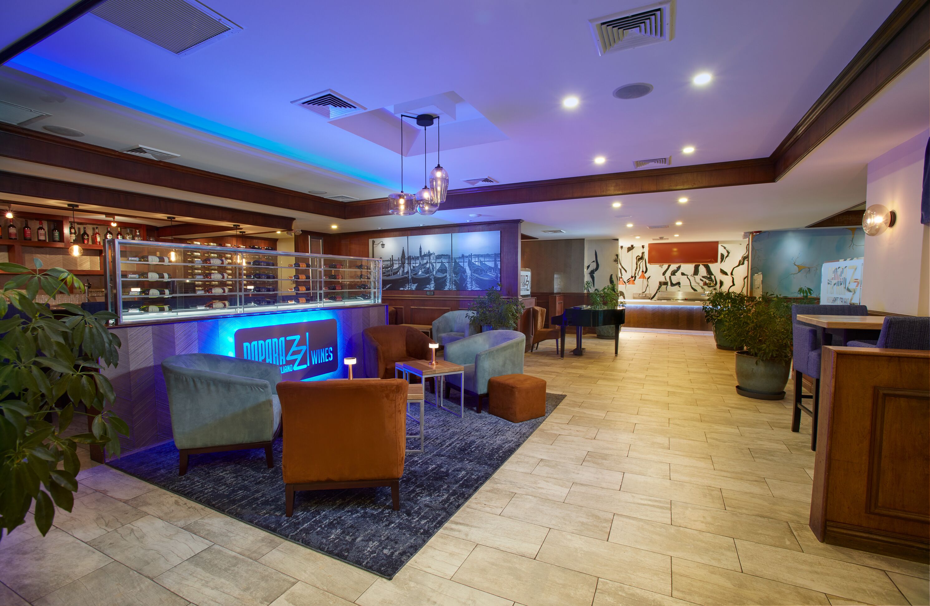 A modern hotel lobby with a bar area, seating arrangements, and a large cityscape painting on the wall.