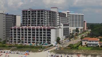 Een hotel aan het strand met meerdere verdiepingen, een zandstrand ervoor en een heldere lucht.