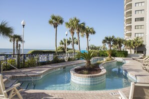 Relax by the serene pool surrounded by palm trees and a well-maintained hedge.
