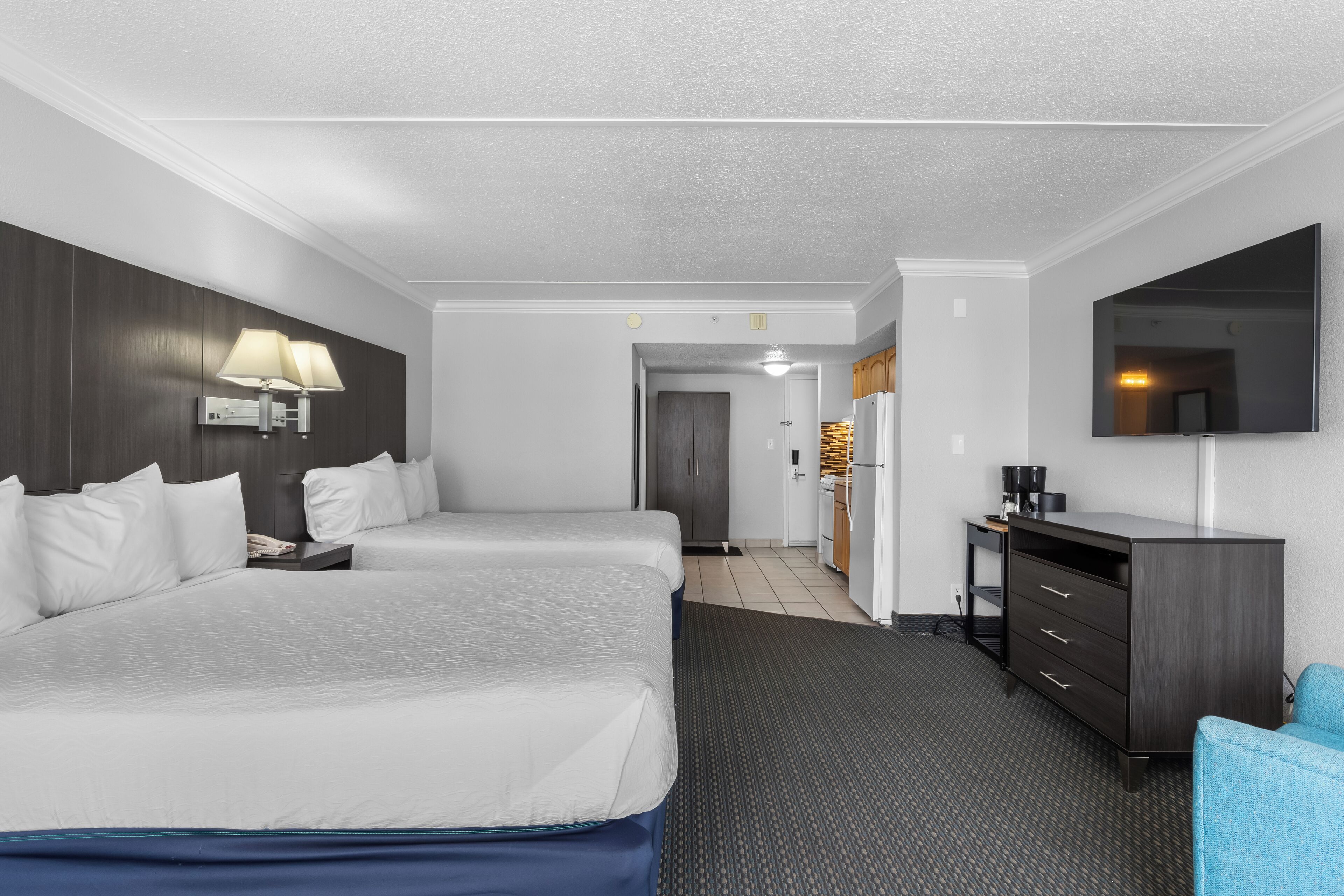 A hotel room with two beds, a desk, a chair, a flat-screen TV, and a minibar.