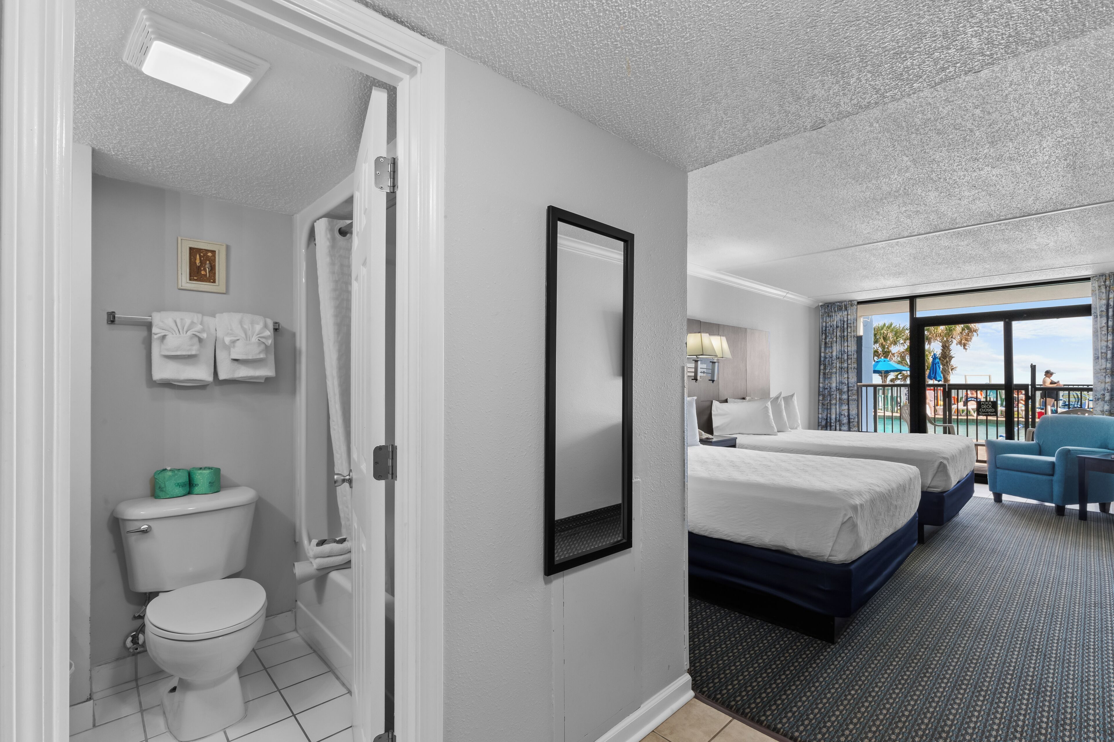 Habitación de hotel con baño, dos camas, balcón con vistas y un ventanal grande.