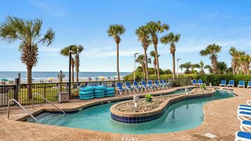 A pool area with lounge chairs, a shallow water section, and a view of the beach.