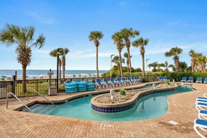 A pool area with lounge chairs, a shallow water section, and a view of the beach.
