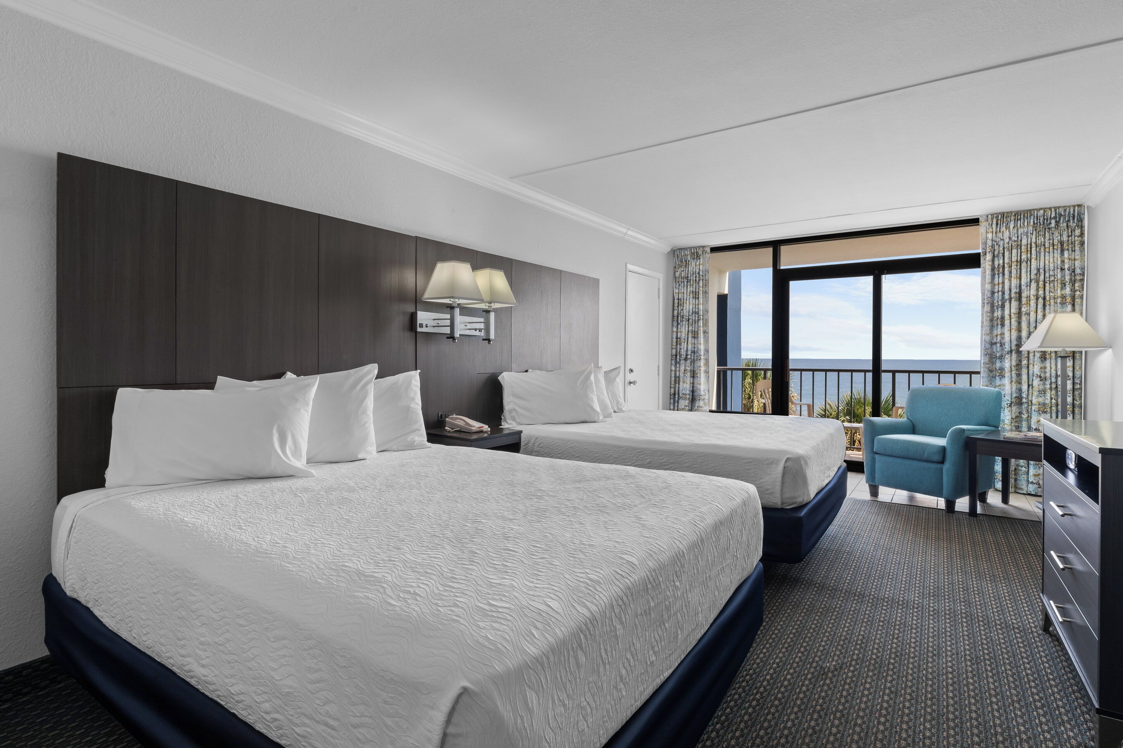 A hotel room with two beds, a desk, a chair, and a large window with a view.