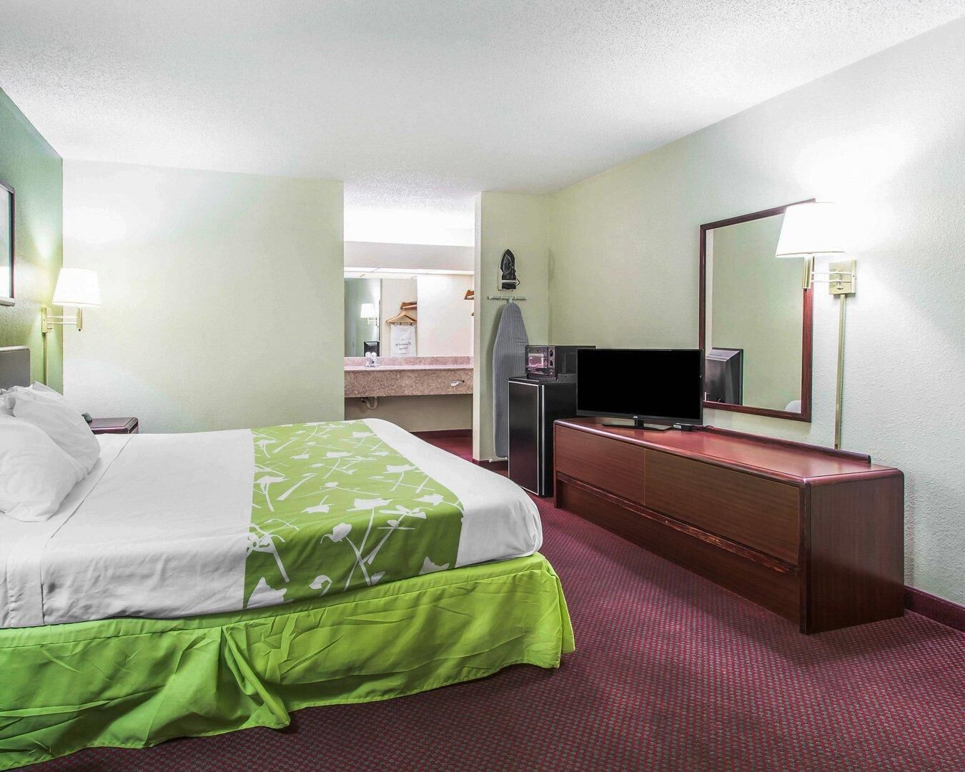 A hotel room with a bed, a TV, a dresser, and a mirror.