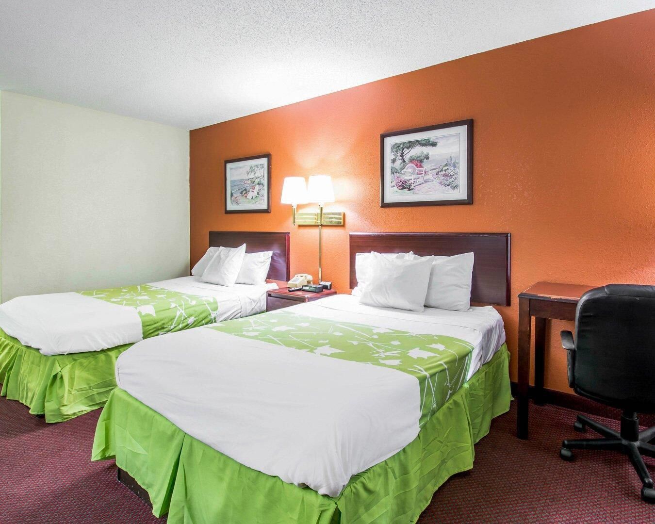 A hotel room with two beds, a desk, a chair, and two wall-mounted lamps.