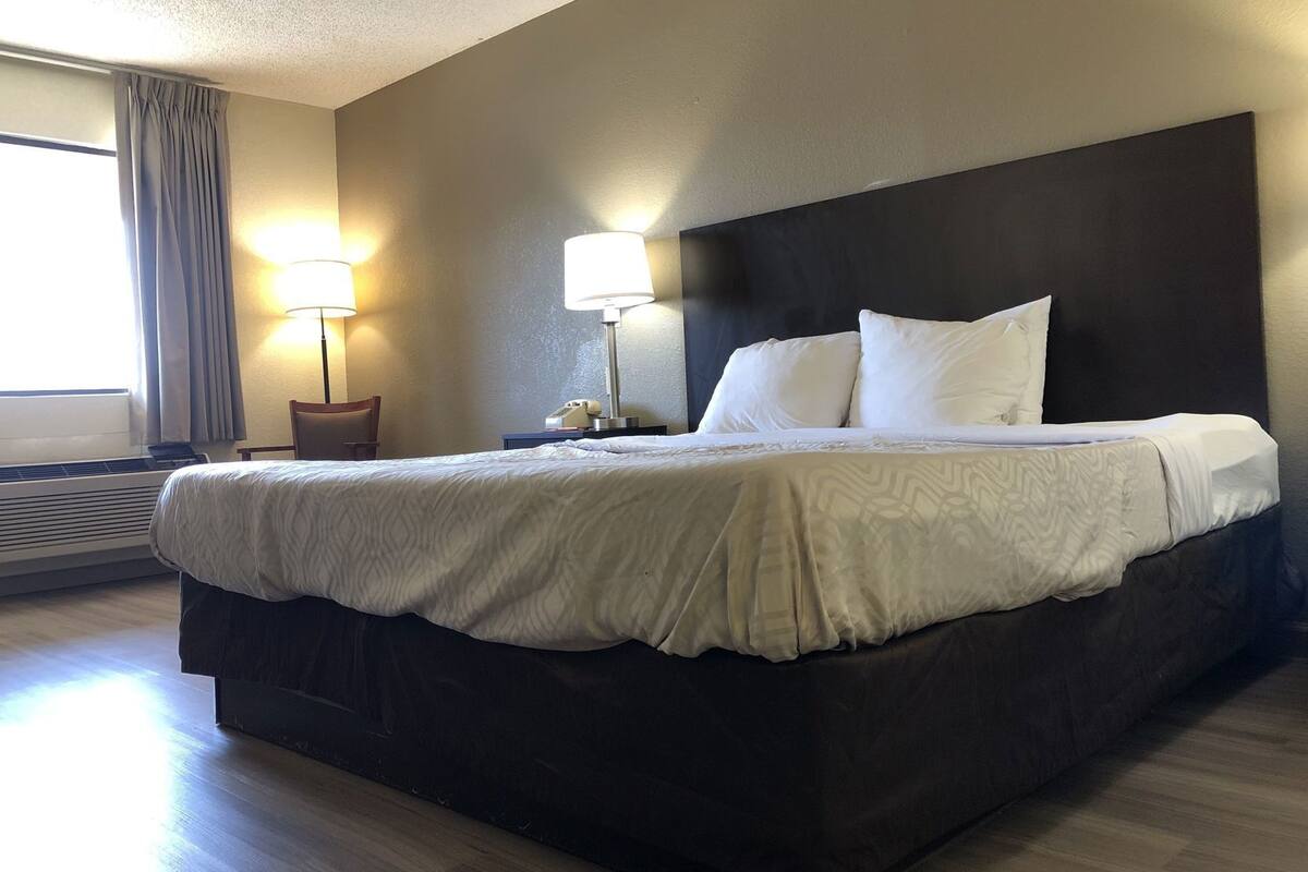 Una habitación de hotel con una cama grande, dos lámparas de noche, una silla y una ventana con cortinas.
