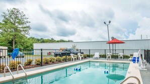 A swimming pool with a metal fence, lounge chairs, and a red umbrella. - Econo Lodge Dothan West (Dothan)