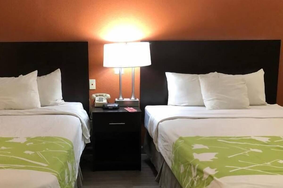 Una habitación de hotel con dos camas, una mesita de noche con lámpara y teléfono.