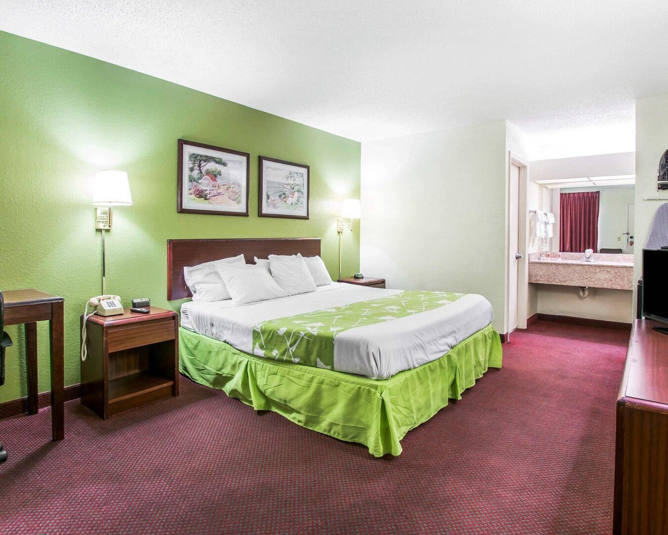 A hotel room with a bed, bedside lamps, a telephone, a mirror, and a television.