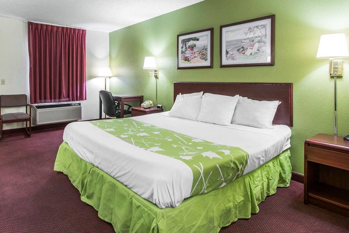 Habitación de hotel con cama, escritorio, silla, dos lámparas de pared y una ventana con cortinas.